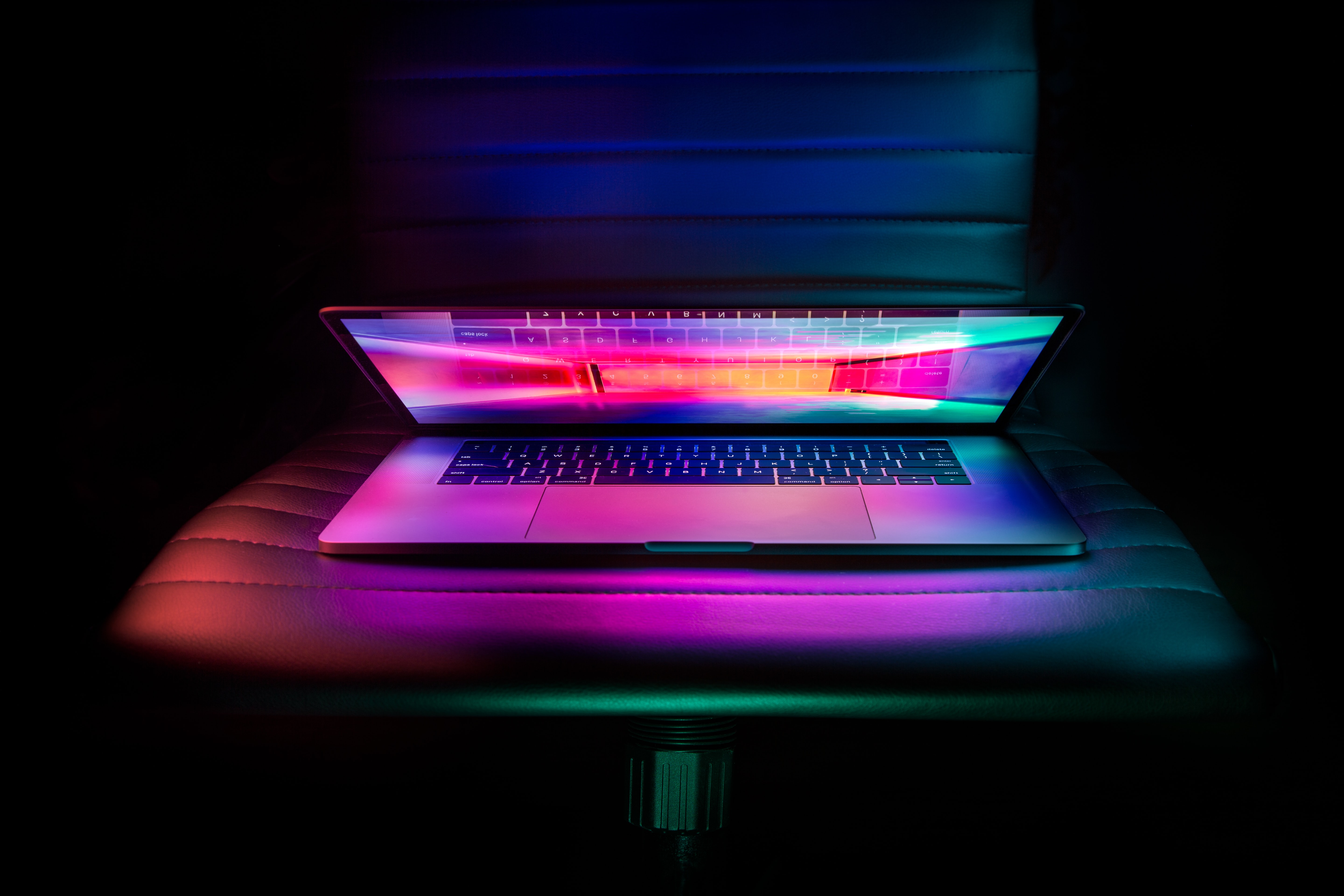partially open laptop resting on a leather chair glowing in the dark